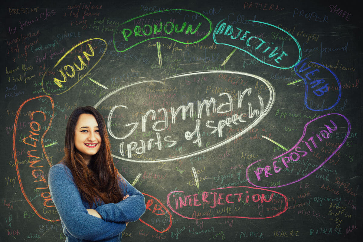 English grammar words written on a chalkboard with a teacher standing in front of it